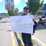 Yan C. Warinussy, SH dan istri memegang poster mempertanyakan perkembangan penanganan kasus penembakan yang dialaminya 3 bulan lalu di Jl. Yos Sudarso, Sanggeng, Manokwari, Kamis (17/10). Foto: IST