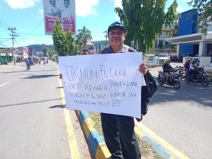 Yan C. Warinussy, SH dan istri memegang poster mempertanyakan perkembangan penanganan kasus penembakan yang dialaminya 3 bulan lalu di Jl. Yos Sudarso, Sanggeng, Manokwari, Kamis (17/10). Foto: IST